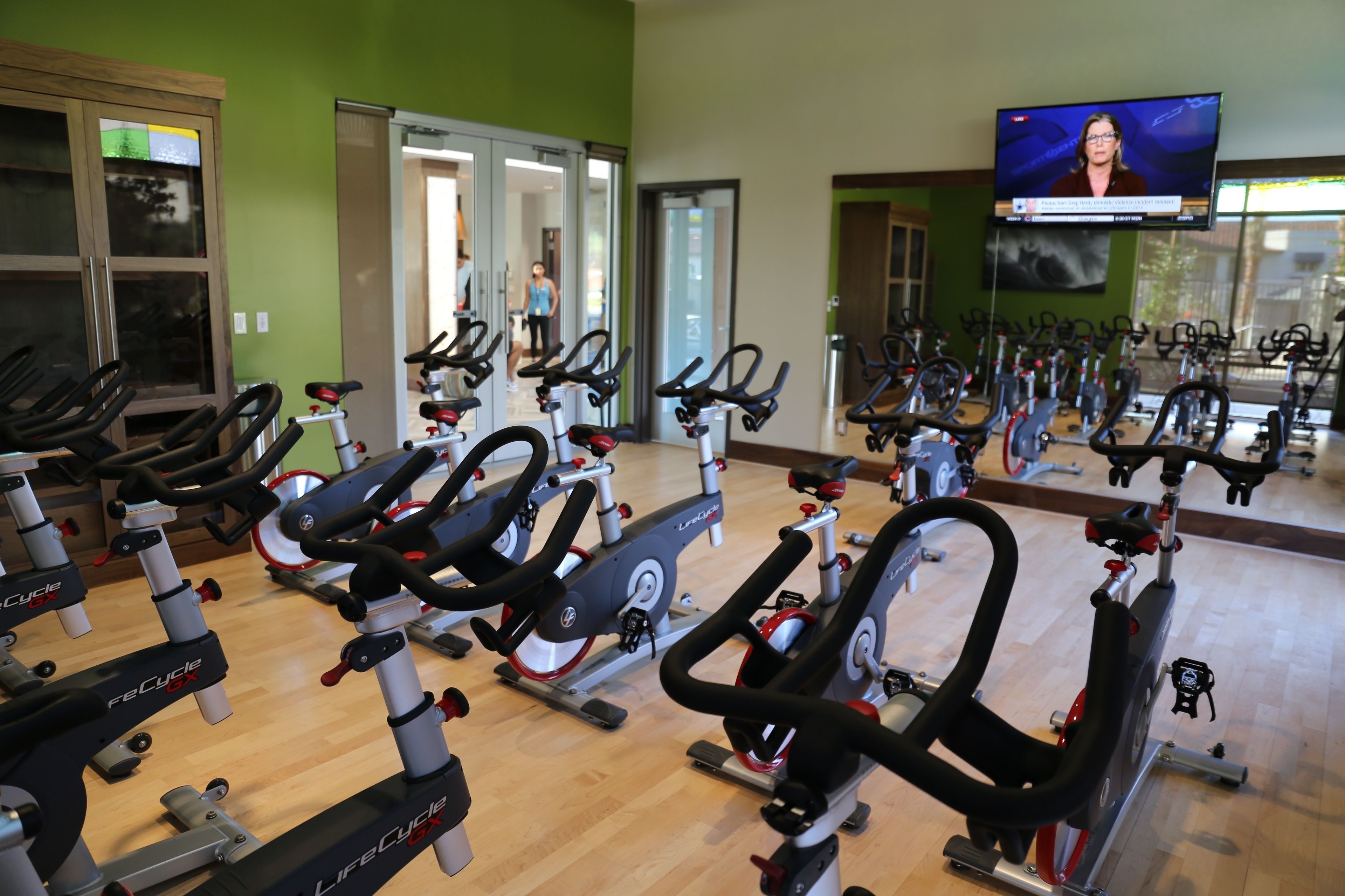 Una palestra con diverse cyclette, uno schermo televisivo e una parete verde.