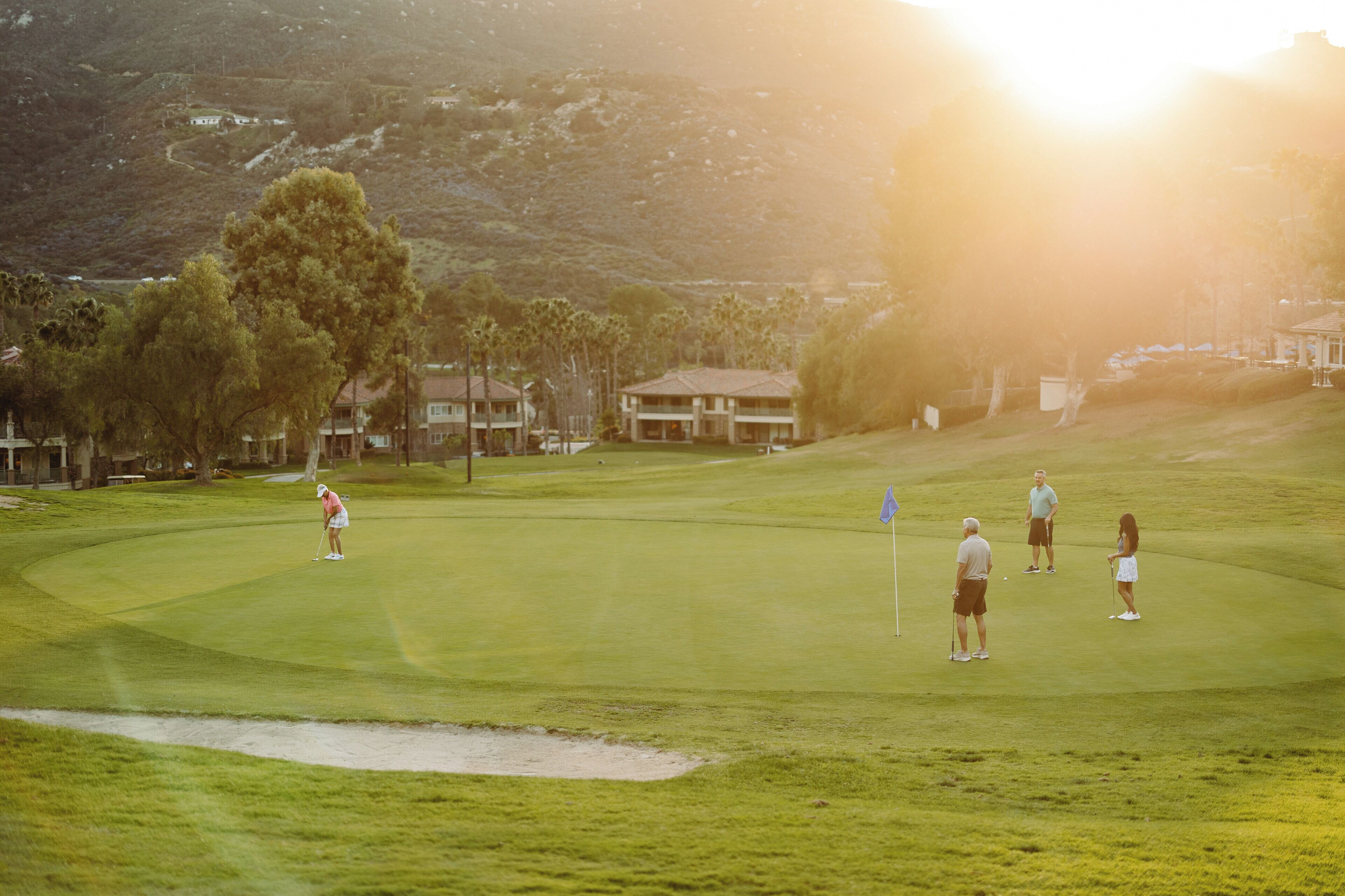 Un parcours de golf avec un tracé bien défini, un bunker de sable et un club-house en arrière-plan.