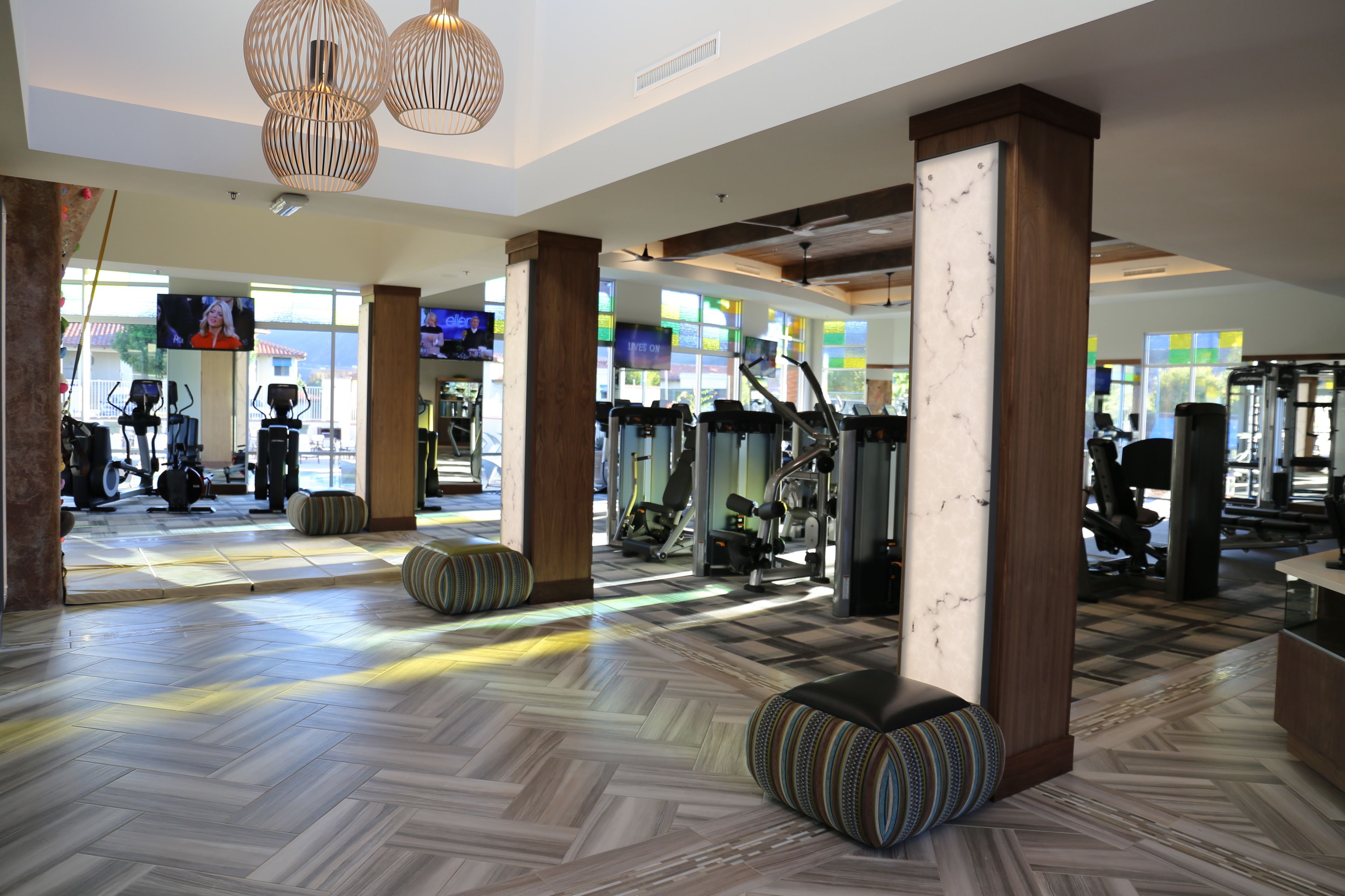 Une salle de sport spacieuse, équipée de matériel d’exercice, avec des piliers en bois et un revêtement de sol à motifs.