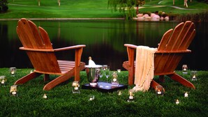Two wooden Adirondack chairs facing a body of water with a grassy area and trees in the background. - Hyatt Vacation Club at The Welk, San Diego Area (Escondido)