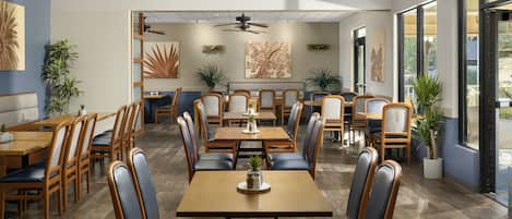A spacious restaurant with multiple dining areas, ceiling fans, and large windows.