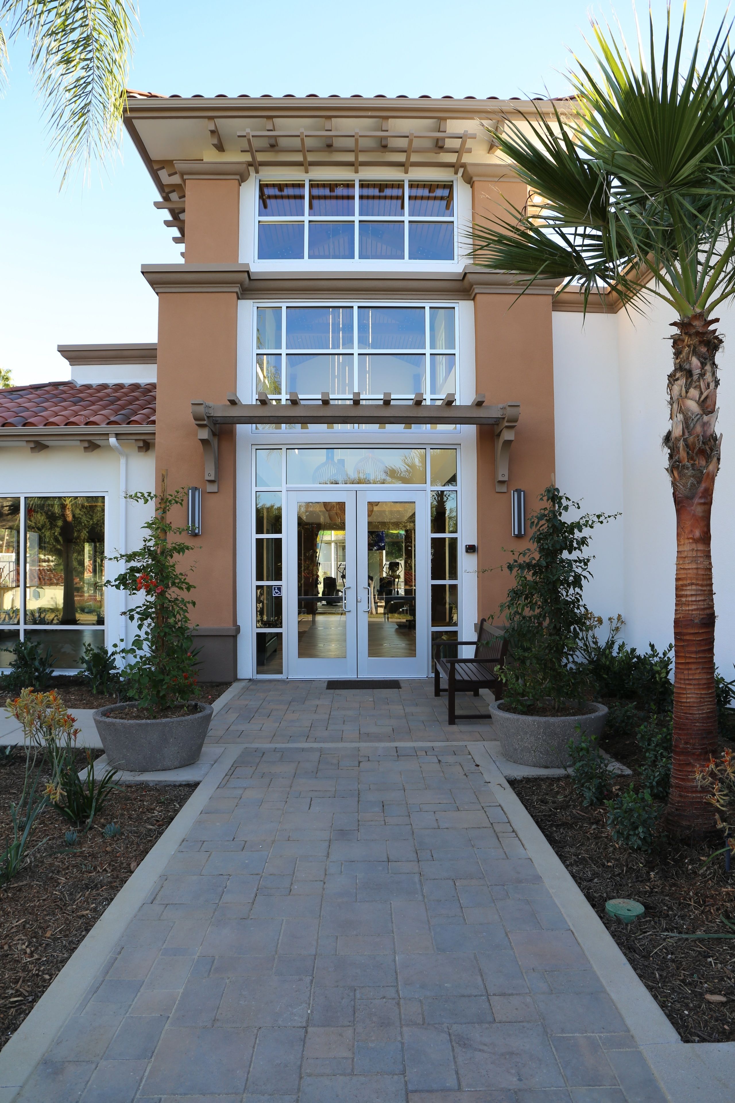 A two-story building with a central entrance, a covered patio area, and potted plants.