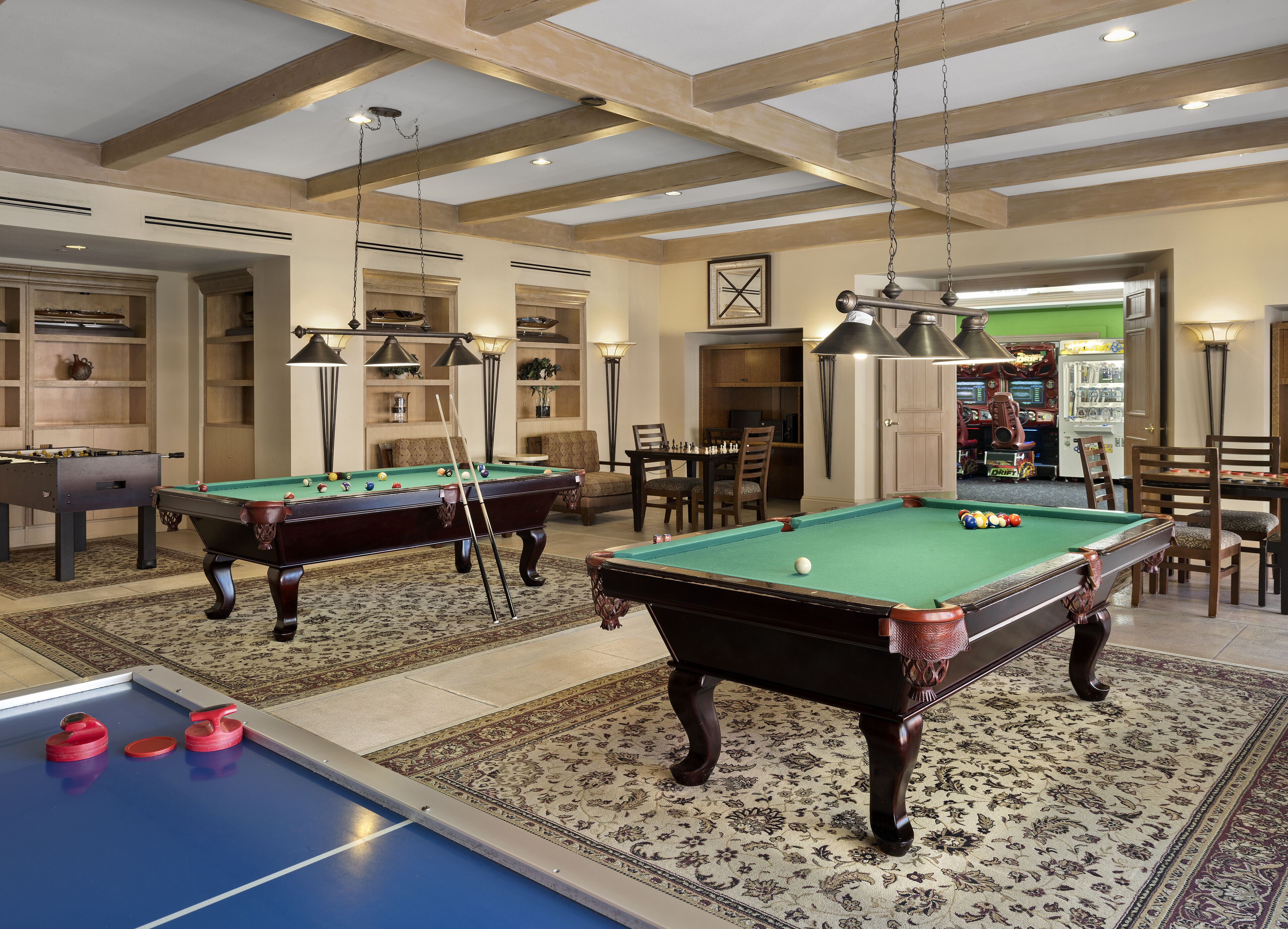 Una sala de billar con dos mesas de billar, una mesa de futbolín y una zona de bar.