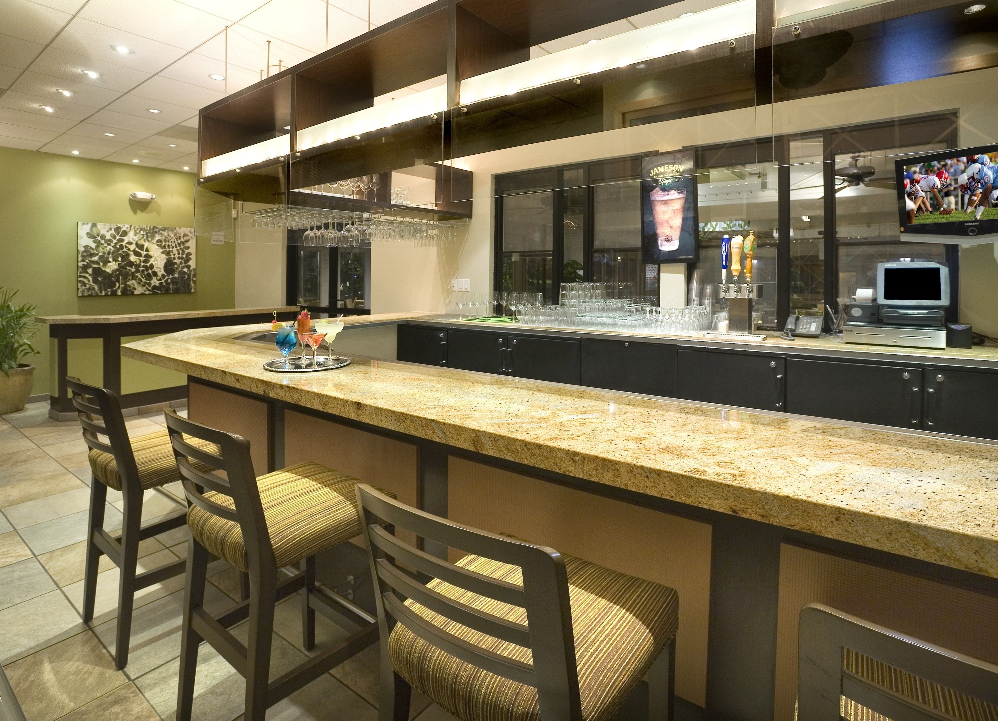 A bar area with a granite countertop, bar stools, and a television screen displaying a sports event.
