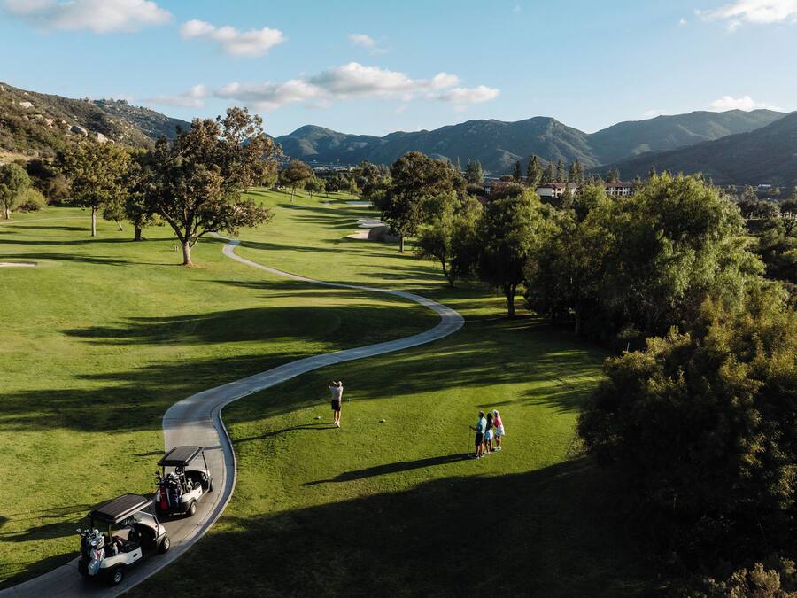 Ein Golfplatz mit gewundenem Weg, einem Golfwagen und einer Person, die gerade geht.