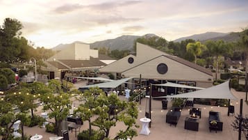 Un espace extérieur aménagé en terrasse, avec des tables et des chaises, entouré d’arbres et offrant une vue sur les montagnes.
