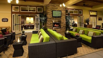 A spacious lounge area with green sofas, wicker furniture, a stone fireplace, and a television mounted on the wall.