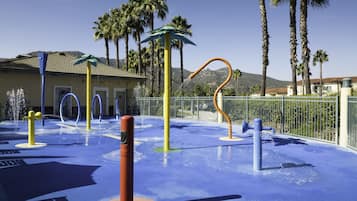 An outdoor water play area with a blue rubber surface, water jets, and a yellow pole.