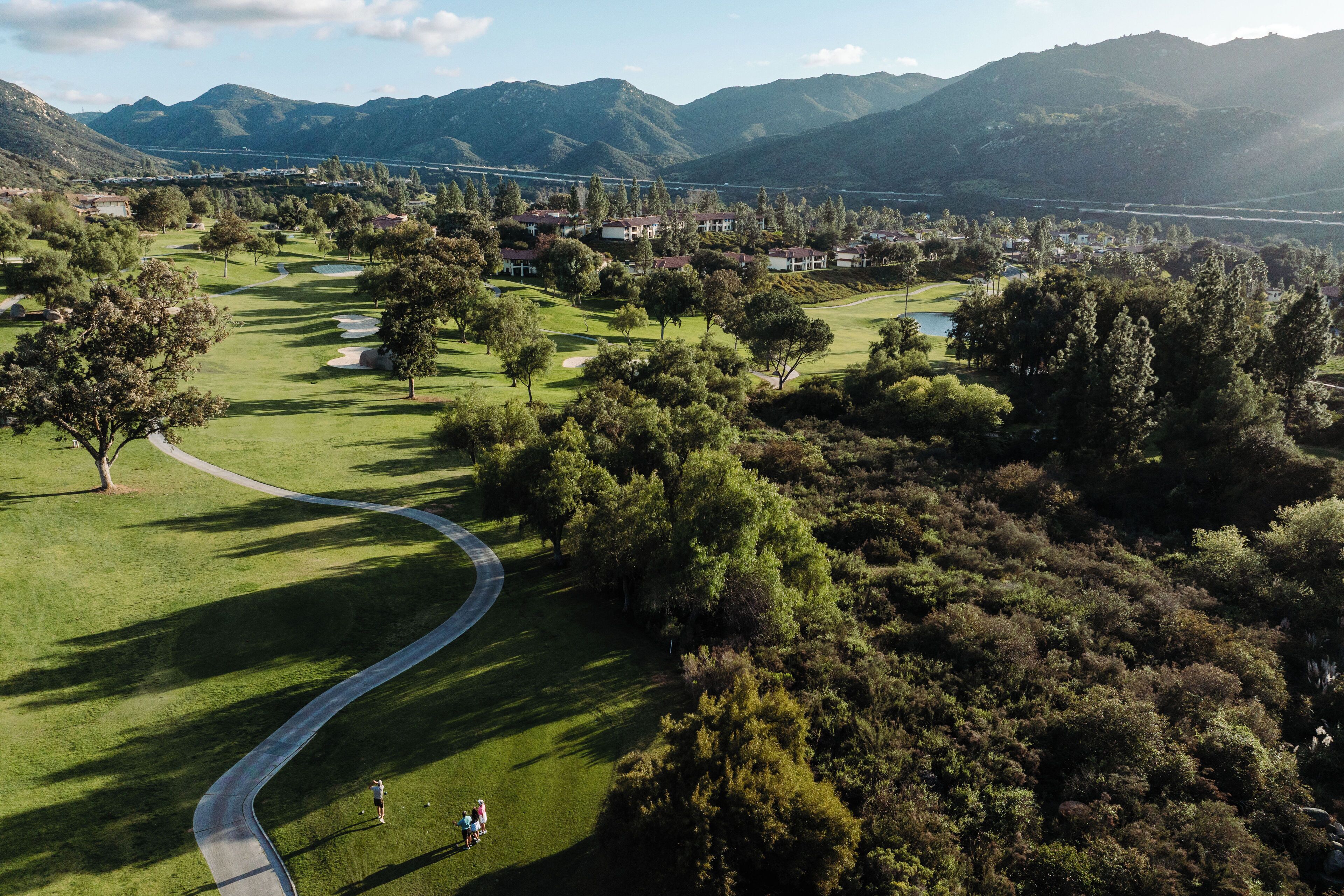 Un parcours de golf avec un chemin sinueux, bordé d’arbres et entouré de collines.