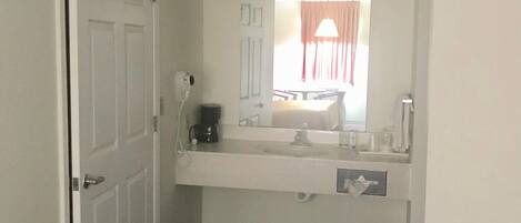 A hotel bathroom with a white sink, mirror, and a small trash can.