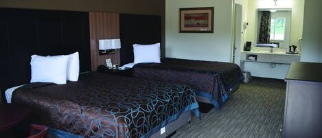 A hotel room with two beds, a desk, a chair, a mirror, a sink, and a window.