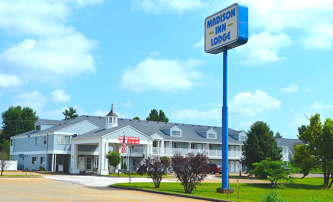 Un motel de dos pisos con un cartel que anuncia 'Madison Inn Lodge' y un letrero que indica 'Nueva Administración'.