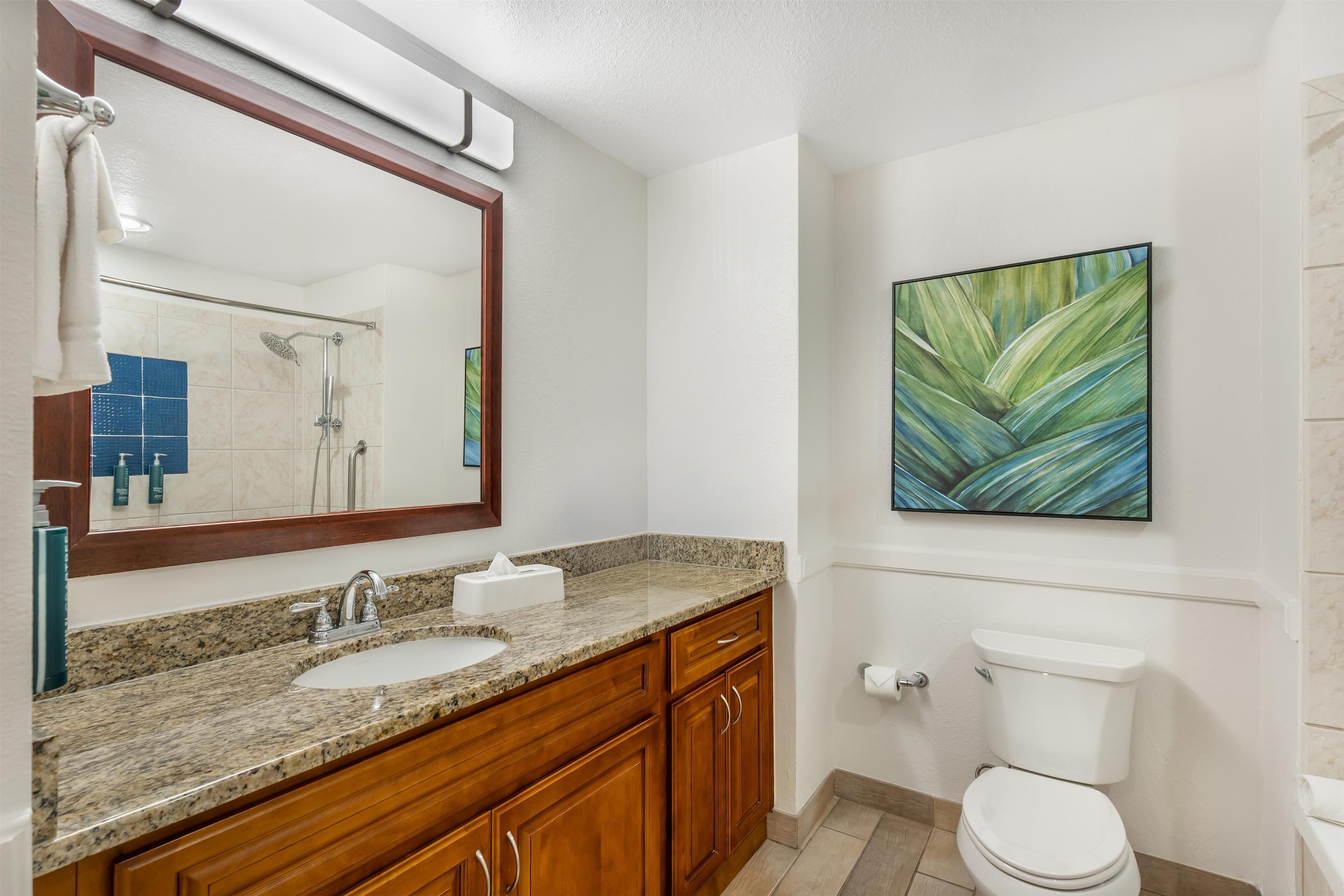 Une salle de bain avec un lavabo sur un plan de travail en granit, des meubles en bois, des toilettes blanches et un grand miroir.