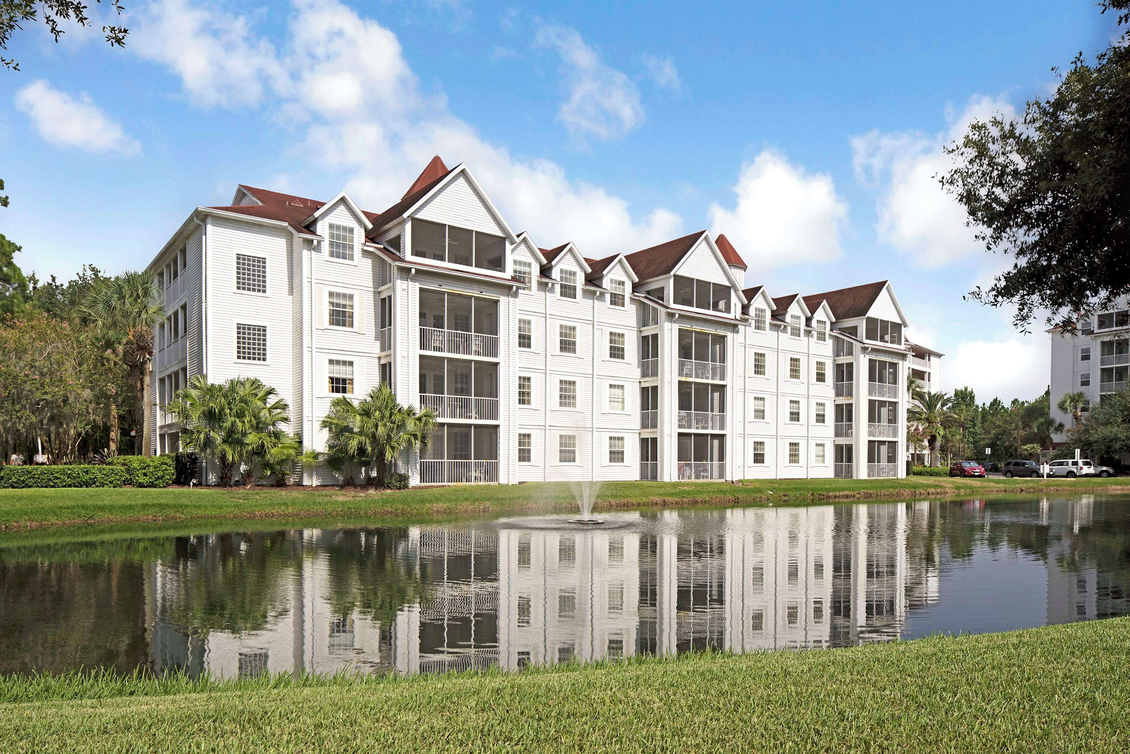 A large, multi-story hotel with a symmetrical facade, a central courtyard with a fountain, and a reflection in the water.
