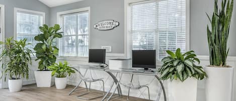 A modern office space with two desks, two chairs, and large potted plants.
