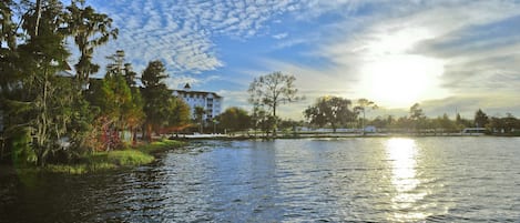 A calm river with a house on the left bank and trees in the background.