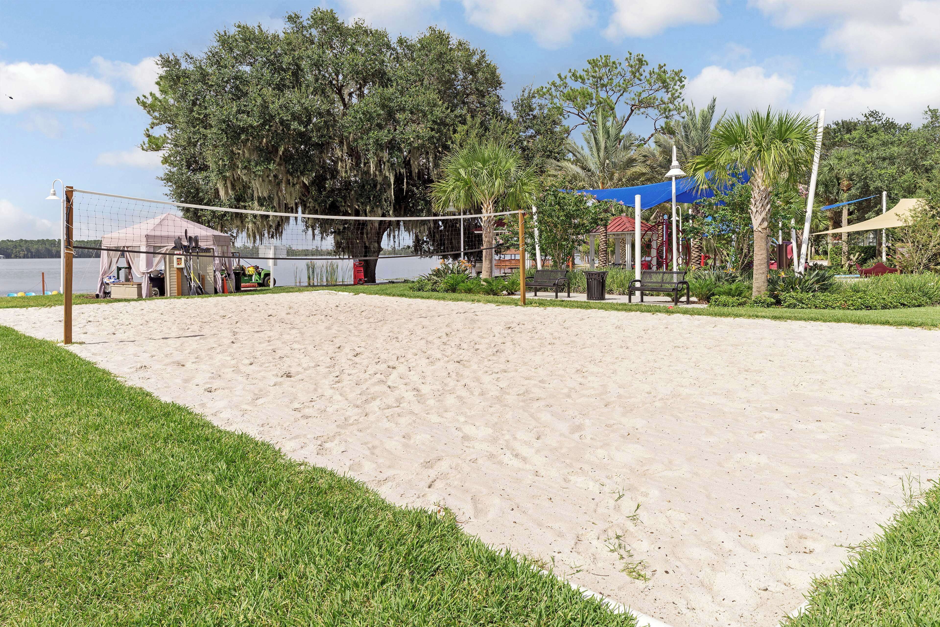 A beach volleyball court with a net, surrounded by sand and grass.