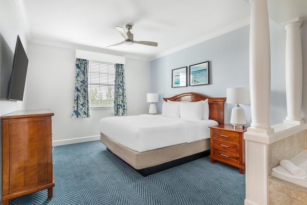 Una habitación de hotel con una cama, una mesita de noche de madera, un televisor, una ventana con cortinas y un ventilador de techo.