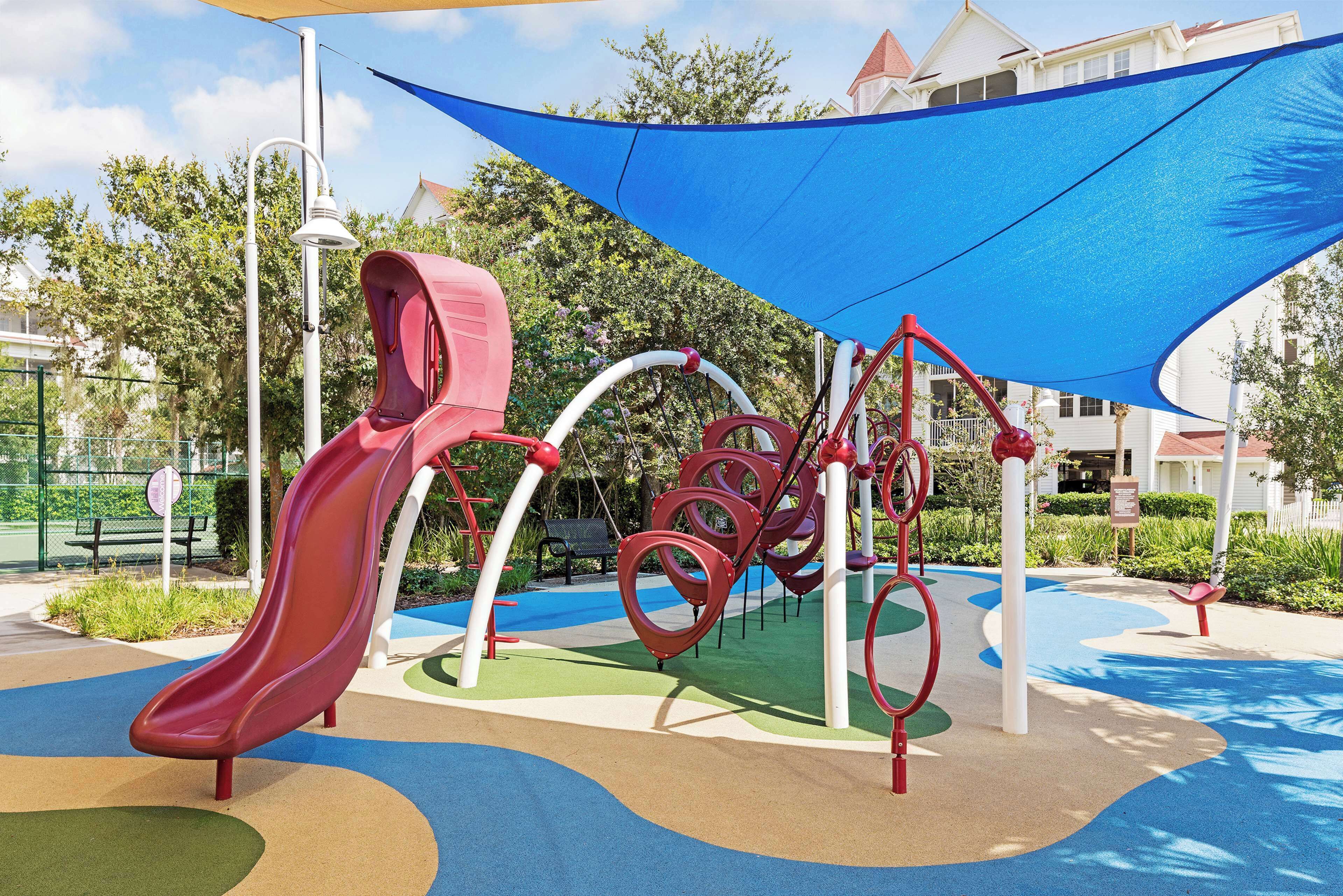 A playground with a red slide, climbing structures, and a shaded area.
