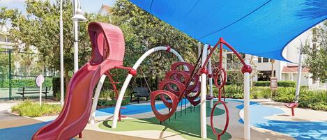 A playground with a red slide, climbing structures, and a shaded area.