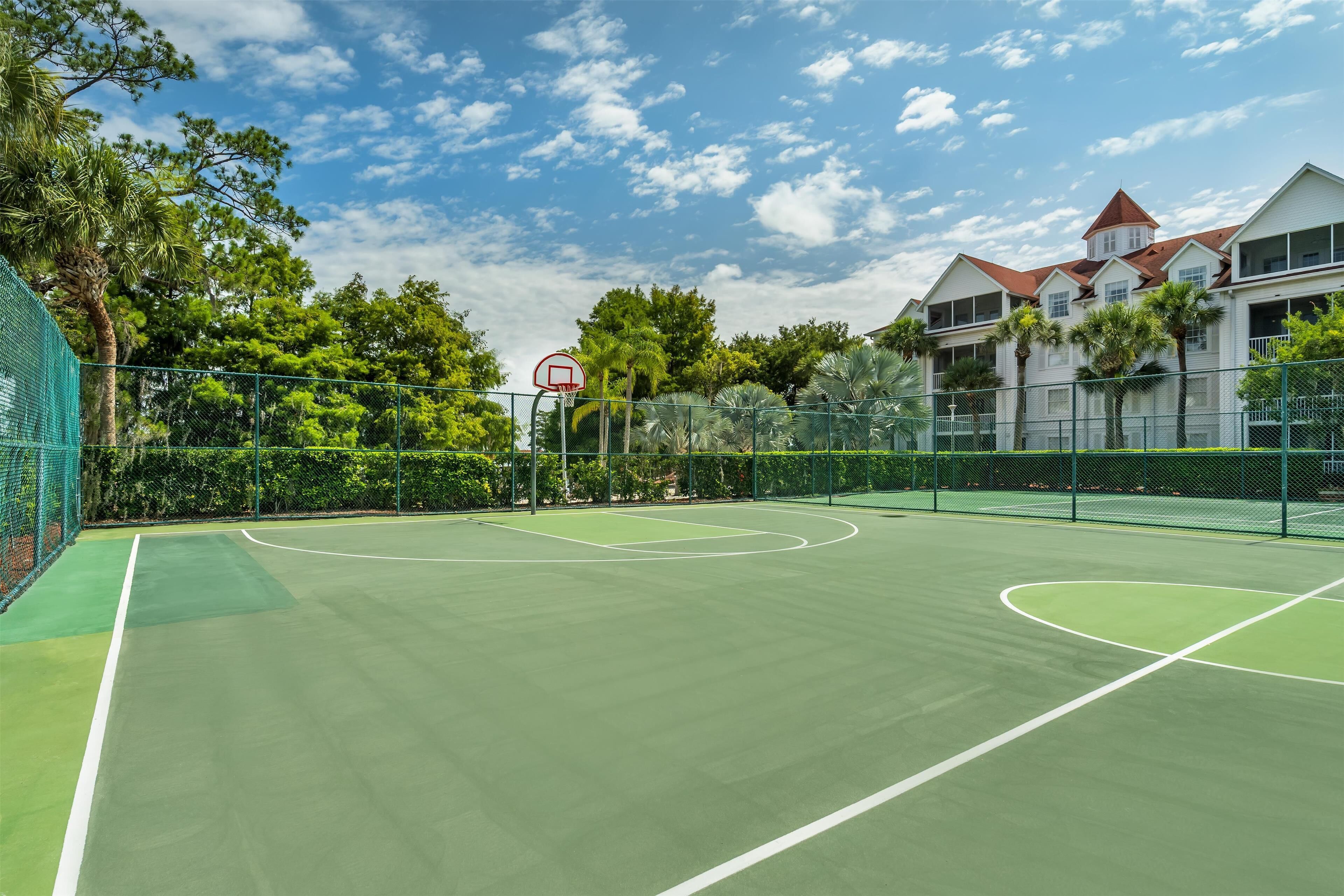 A tennis court with a net, surrounded by a fence and trees.