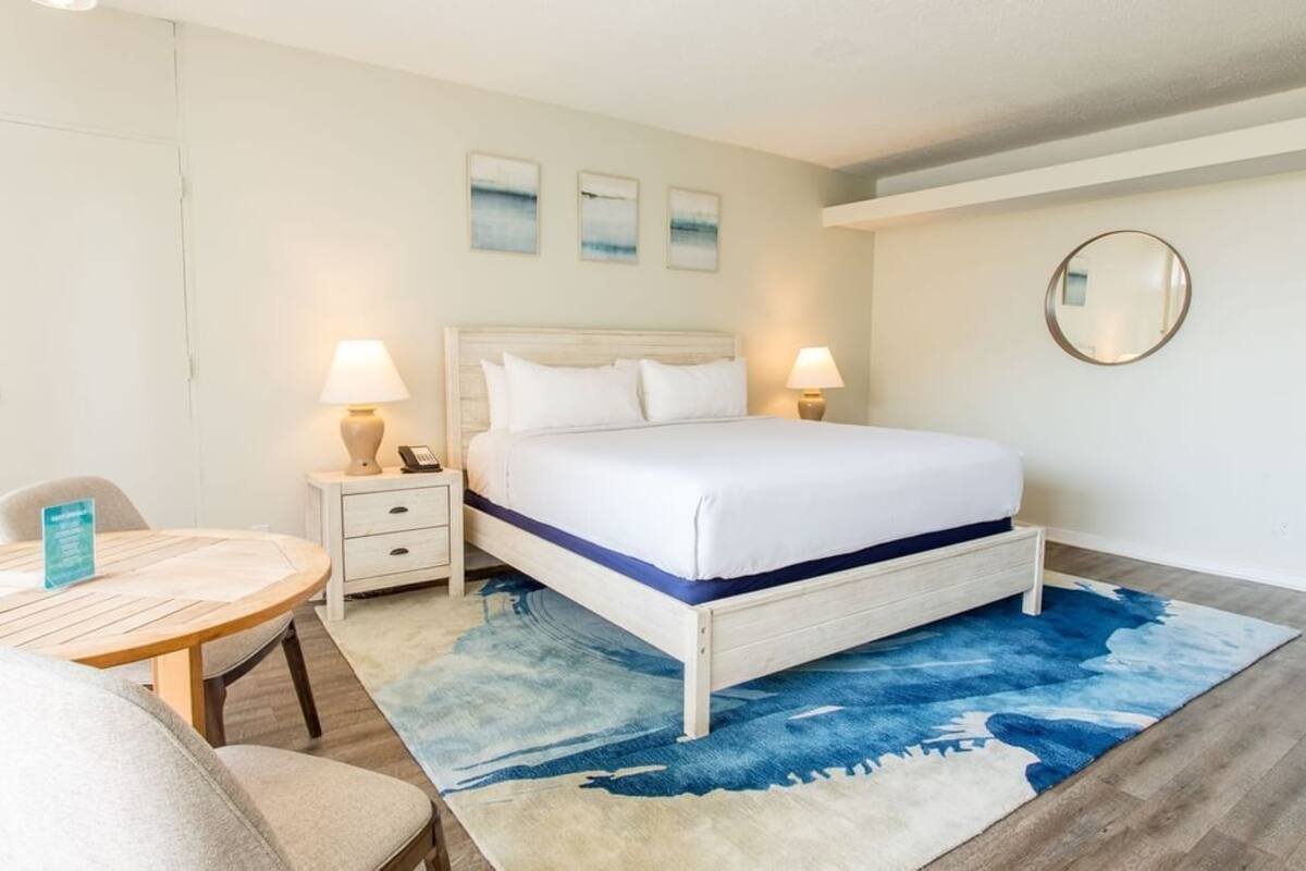 Habitación de hotel con cama, mesitas de noche, un espejo redondo y una pequeña mesa con sillas.