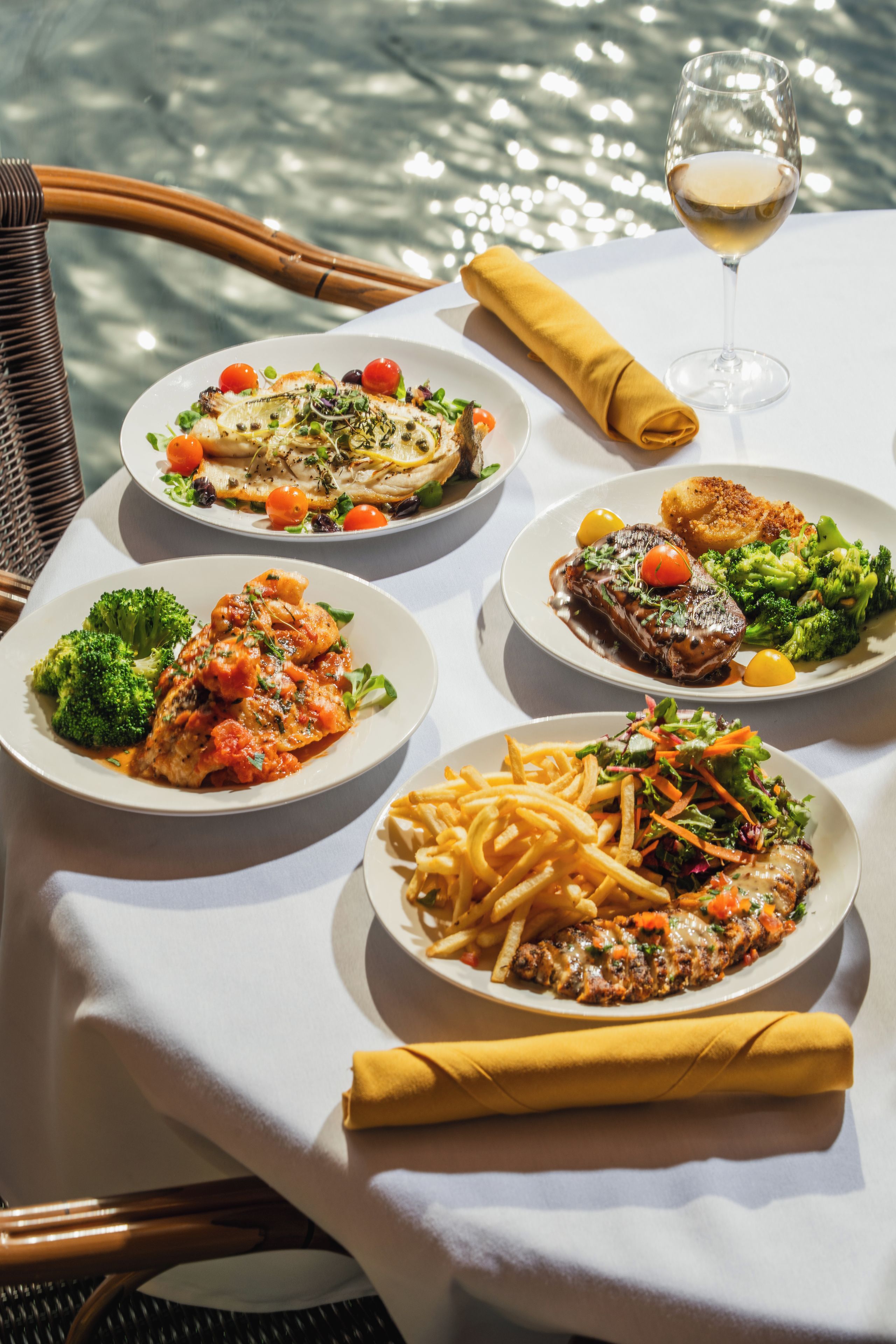 A table set with various dishes including pasta, steak, and vegetables, with a glass of wine and a napkin.