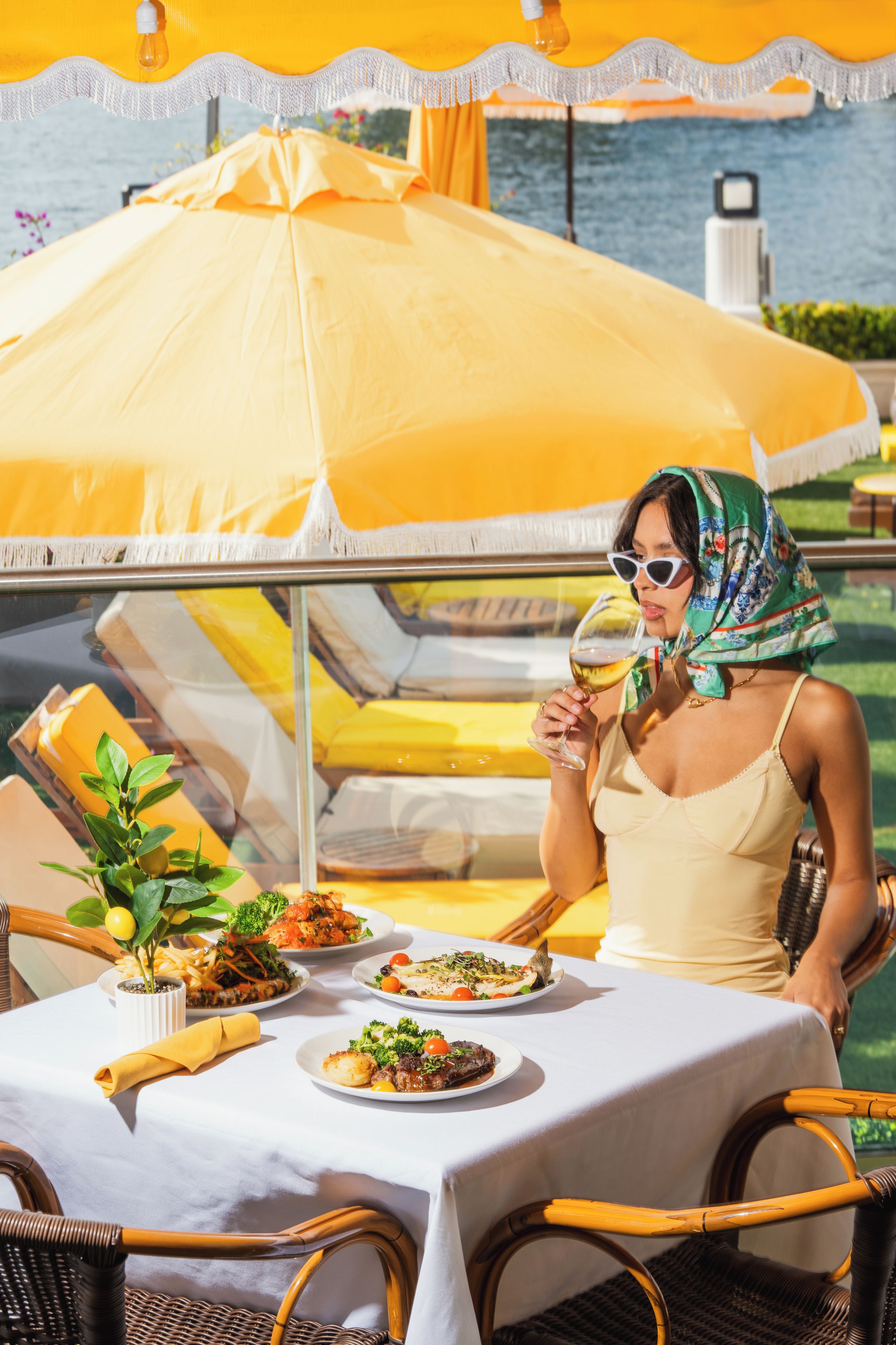 A dining table with plates of food, a person holding a glass, and a yellow umbrella.
