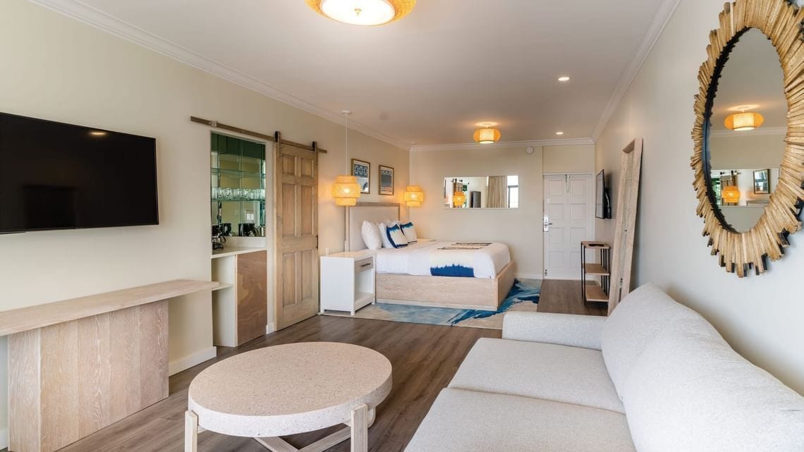 Una habitación de hotel con cama, sofá, una mesita redonda, televisor y espejo.