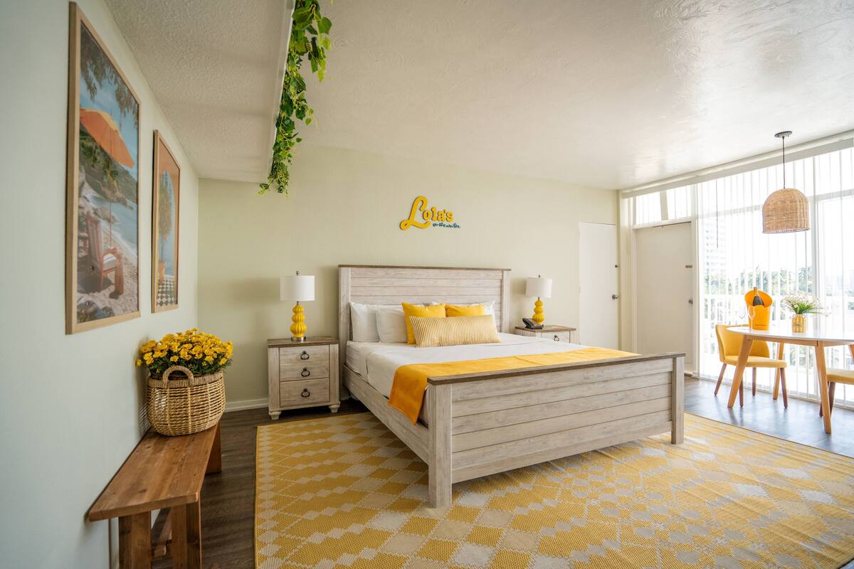 Un dormitorio con cama, mesitas de noche, un banco, una cesta de flores y un cartel en la pared.