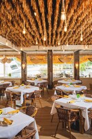 A restaurant with multiple tables, wicker chairs, and hanging light fixtures.