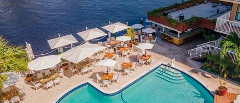 An aerial view of a resort with a swimming pool, outdoor seating, and a view of the sea.
