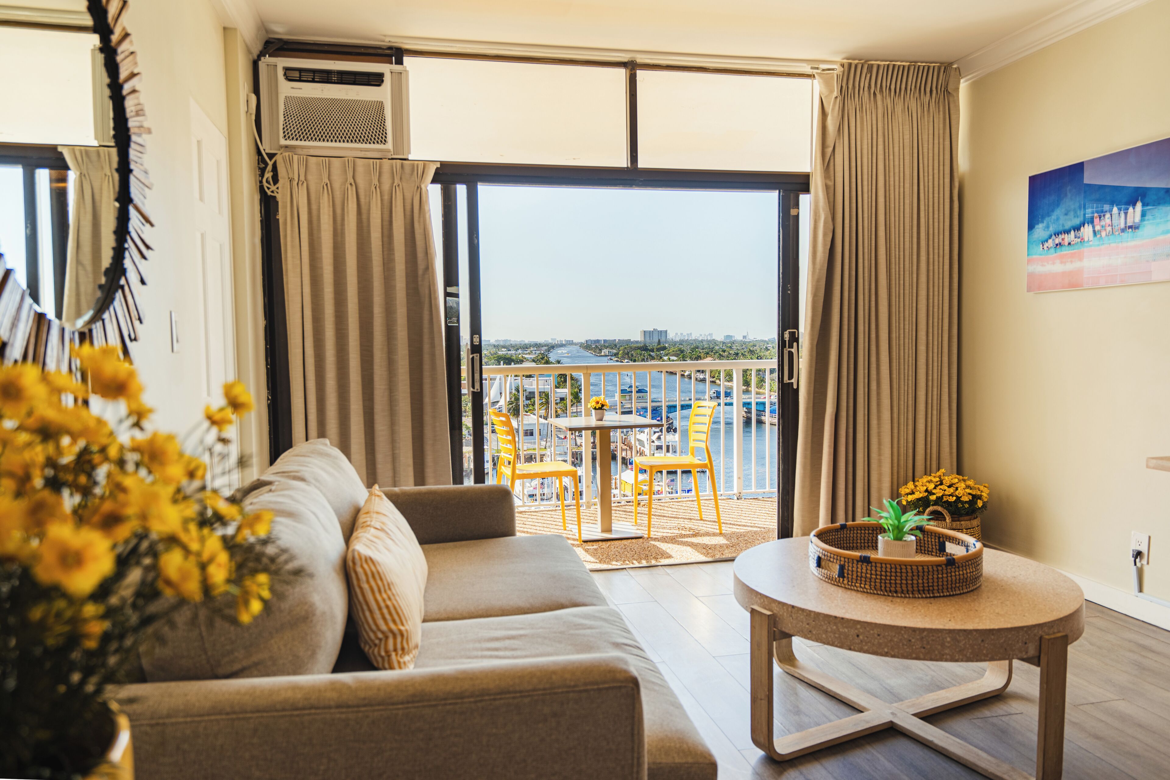 Un salon moderne avec un canapé, une table basse et une vue sur un balcon aménagé avec du mobilier d’extérieur.