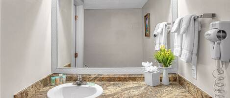 A bathroom with a granite countertop, a white sink, a mirror, a hairdryer, and a vase with flowers.