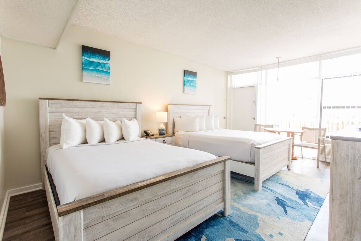 Habitación de hotel con dos camas, un escritorio y un balcón con vistas.