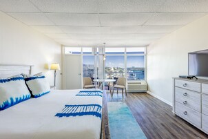Habitación de hotel con una cama grande, televisión, escritorio con sillas y vistas a la ciudad a través de amplias ventanas.