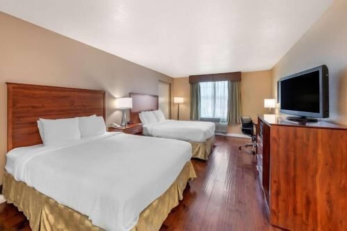 A hotel room with two beds, a television, a desk, and a window with curtains.