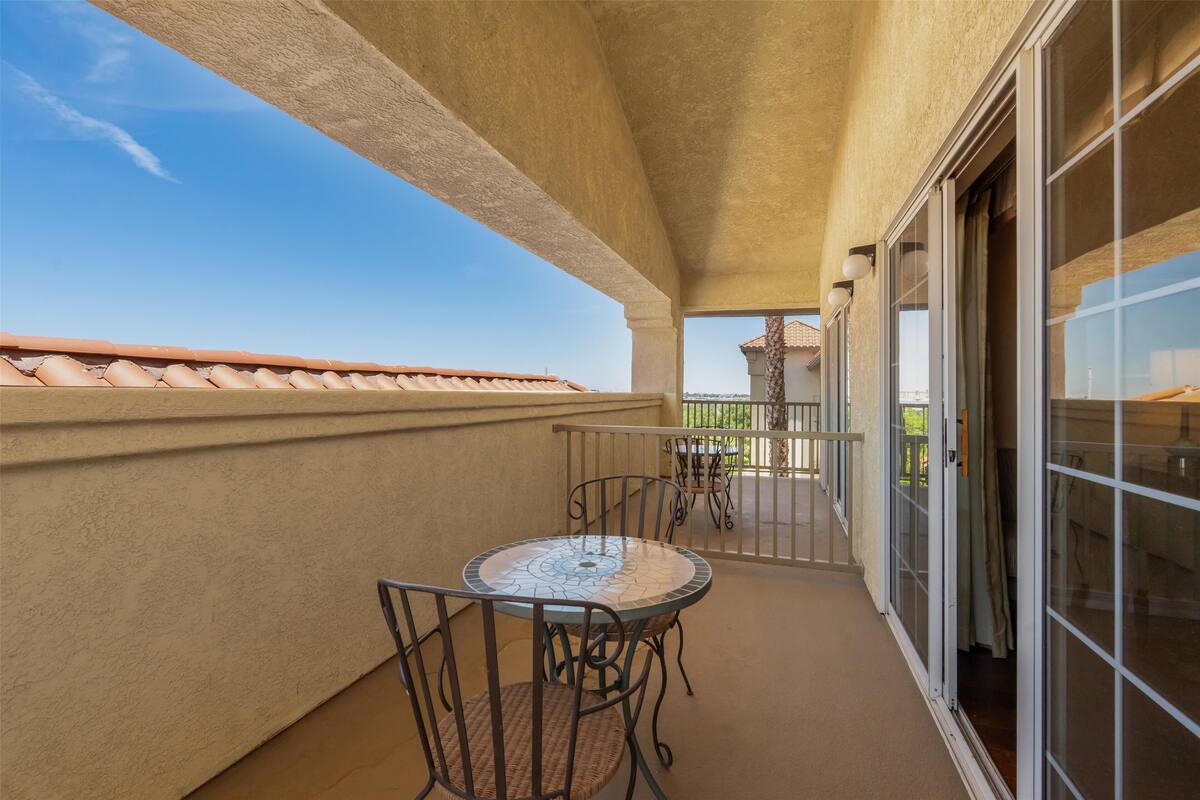 A balcony with a round table and chairs, a view of the sky, and a building in the background.