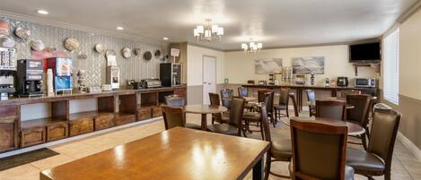 A spacious hotel lobby with a long reception desk, multiple seating areas, and a television mounted on the wall.