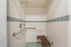 Um espaço de chuveiro pequeno, com azulejos, barra de apoio e banco.