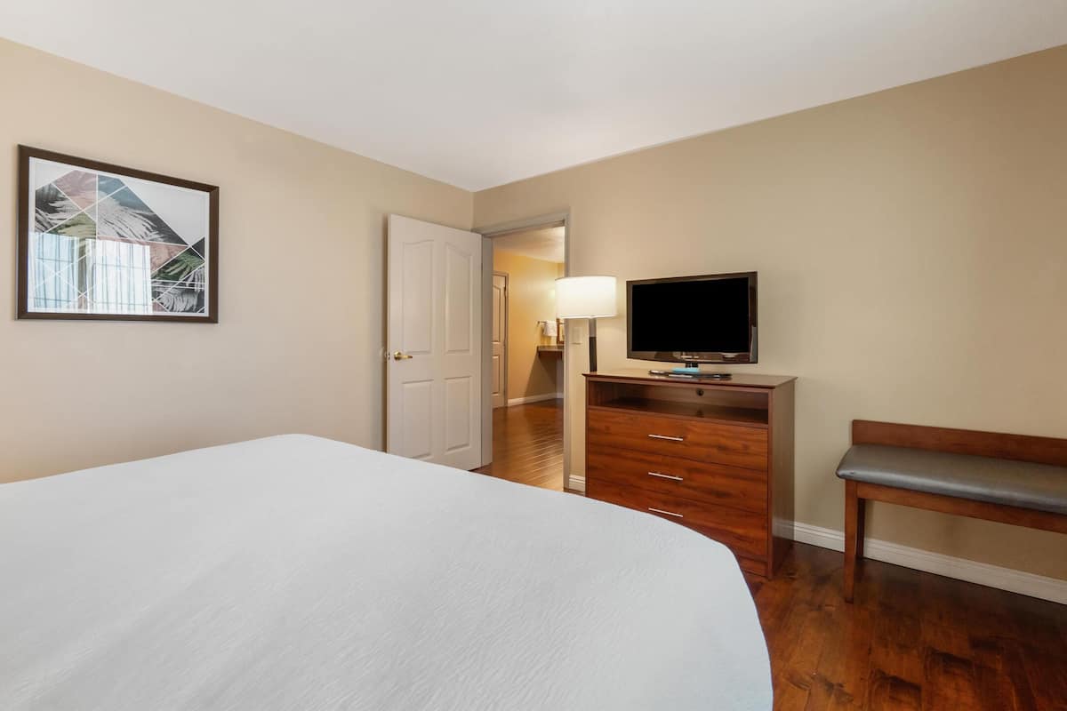 A hotel room with a large bed, a wooden dresser, a television, and a bench.