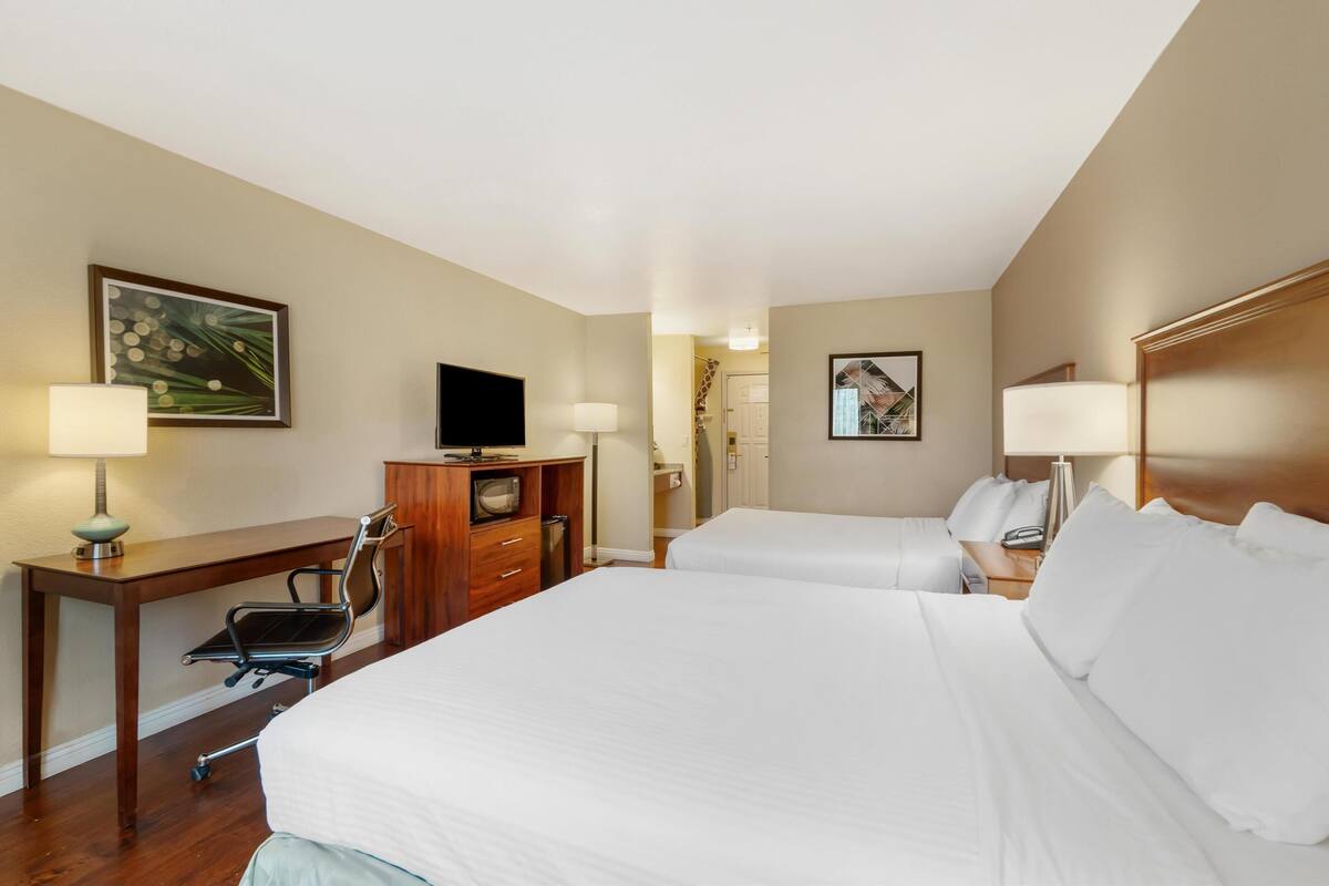 A hotel room with two beds, a desk with a chair, a television, and a wardrobe.