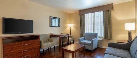 A hotel room with a flat-screen TV, a wooden dresser, a sofa, a chair, a small table, and a lamp.
