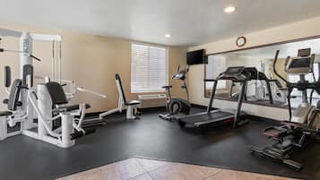 A gym with cardio machines, weight training equipment, and a mirrored wall.
