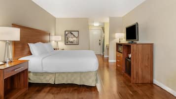 Quarto de hotel com cama de madeira, televisão, secretária com candeeiro e um quadro na parede.