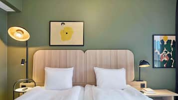 A hotel room with a double bed, two bedside tables, a nightstand, a wall-mounted lamp, and two framed artworks.