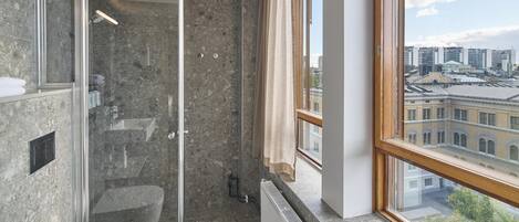 A modern bathroom with a glass shower enclosure, a white toilet, and a view of a cityscape through a large window.