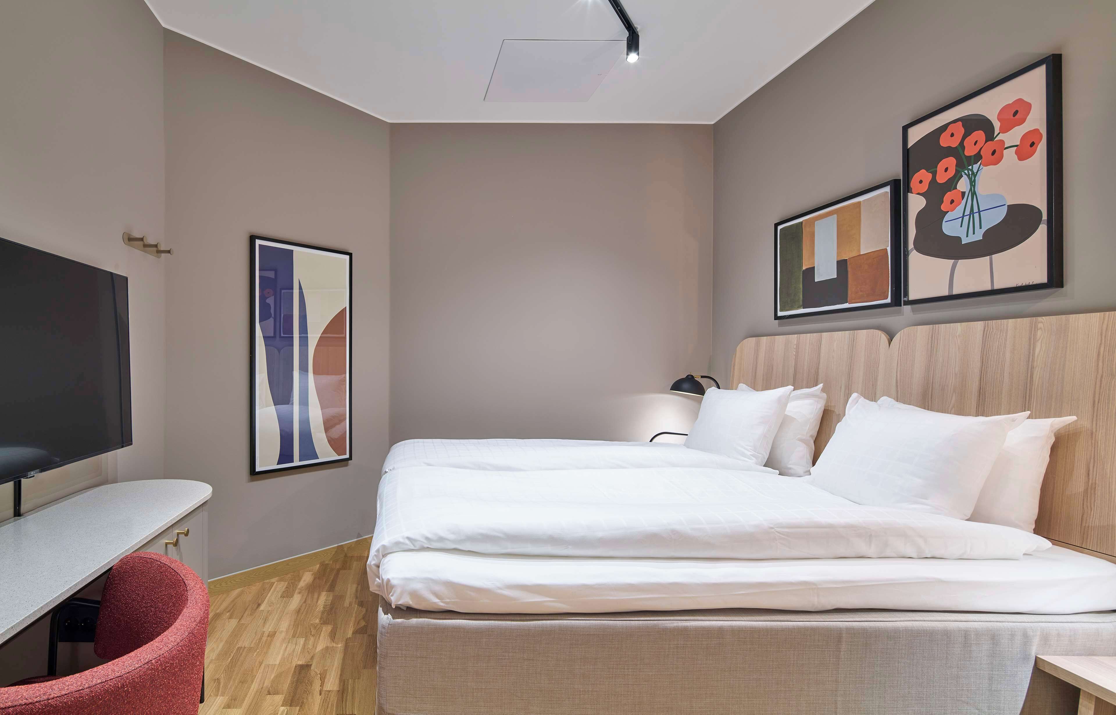 Een moderne hotelkamer met een bed, een bureau, een stoel en kunstwerken aan de muur.