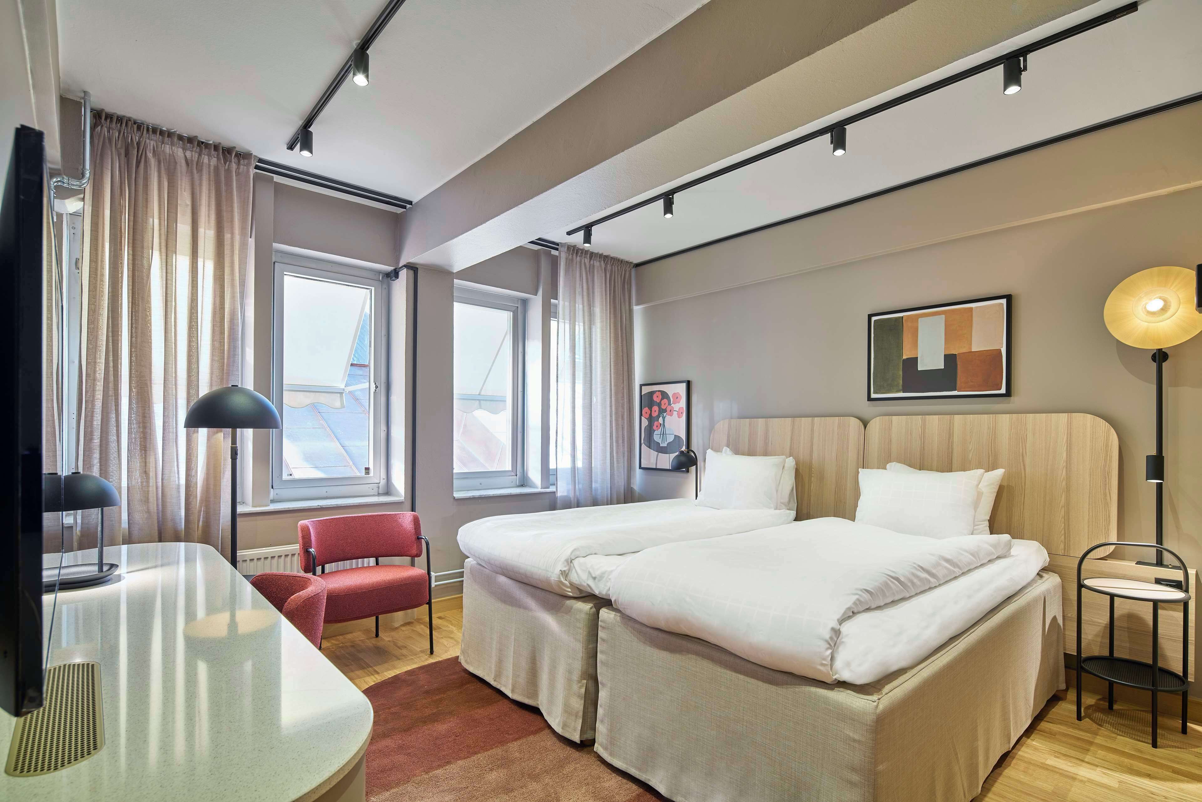 Una habitación de hotel con cama, escritorio, silla, televisor y ventana con cortinas.
