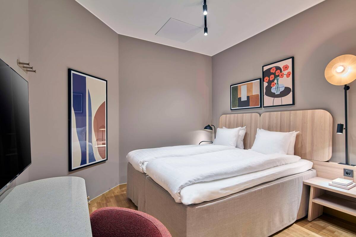 A modern hotel room with a large bed, a flat-screen TV, artwork on the walls, and a bedside lamp.